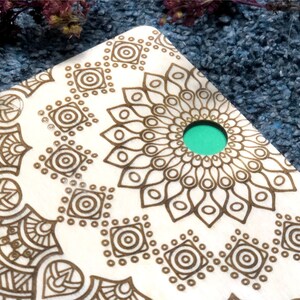 May include: A wooden coaster with a brown mandala design and a teal green circle in the center.