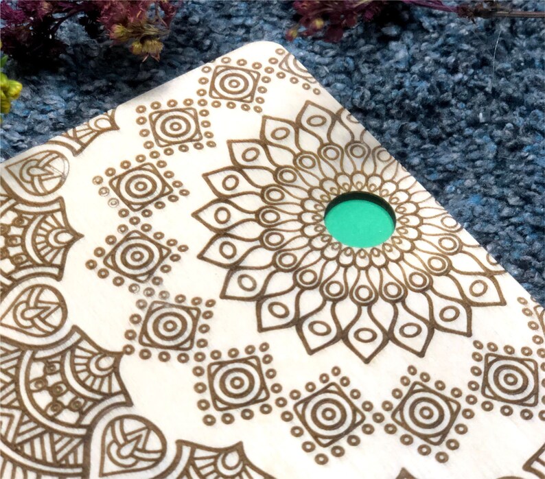 May include: A wooden coaster with a brown mandala design and a teal green circle in the center.