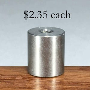 May include: A cylindrical metal spacer with a smooth, brushed silver finish and a threaded hole in the center of the top surface. The object is positioned upright, displaying a uniform metallic texture and a simple, functional industrial design.