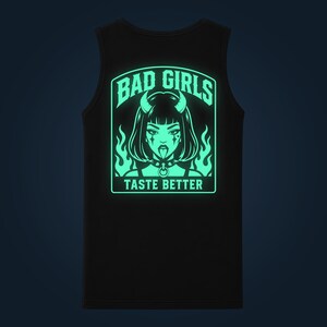 Può includere: Una canotta nera con una grafica verde chiaro luminescente sul retro. Il disegno raffigura una persona con corna, un collare e fiamme, con il testo BAD GIRLS sopra e TASTE BETTER sotto l'illustrazione in un carattere tipografico in grassetto.