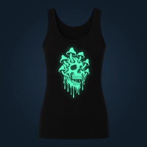 Può includere: Una canotta nera con una grafica centrale raffigurante un teschio umano con funghi che crescono dalla parte superiore e dai lati. Il disegno del teschio e dei funghi è in verde chiaro luminoso, con gocce dall'aspetto liquido sotto la mascella.