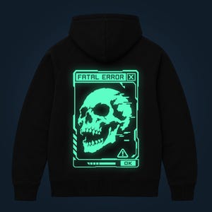 May include: A black hooded sweatshirt featuring a large, glowing mint-green graphic on the back. The design depicts a skull inside a digital interface box with the text FATAL ERROR at the top, a warning icon, and an OK button at the bottom.