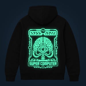 Puede incluir: Una sudadera con capucha negra que presenta un gráfico grande de color verde menta brillante en la parte posterior. El diseño muestra un cerebro estilizado con un ojo central, rodeado de un marco técnico y el texto "SUPER COMPUTER" en negrita.