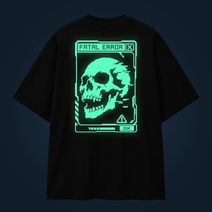 Op de afbeelding: Een zwart t-shirt met korte mouwen en een lichtgevende lichtgroene afbeelding op de achterkant. Het ontwerp toont een schedel in een digitaal vensterkader met de tekst FATAL ERROR bovenaan, een waarschuwingsdriehoek en een OK-knop onderaan.