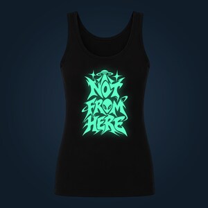 Könnte beinhalten: Ein schwarzes Tanktop mit einer leuchtend hellgrünen Grafik auf der Brust. Das Design zeigt einen stilisierten Alien-Kopf, eine fliegende Untertasse und den Text "NOT FROM HERE" in einer kantigen Schriftart mit vierzackigen Sternen.