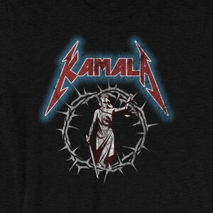 May include: Black t-shirt with a red and white graphic of a figure holding scales of justice in a crown of thorns. The text "KAMALA" is above the figure in a stylized font.