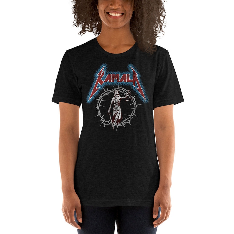 May include: A black t-shirt with a graphic of a woman in a crown of thorns and the word "KAMALA" in a metal font.