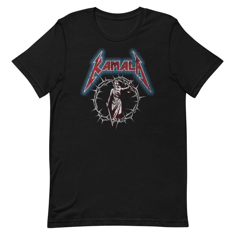May include: Black t-shirt with a red and blue graphic of a woman in a robe holding a scale of justice. The graphic is surrounded by a crown of thorns and the word "KAMALA" is written in a metal font.