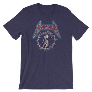 May include: A navy blue t-shirt with a red and white graphic of a figure holding scales of justice, surrounded by a crown of thorns. The text "KAMALA" is above the figure in a red and white font.