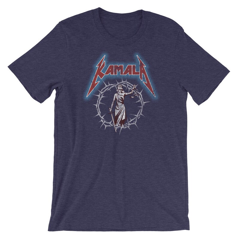 May include: A navy blue t-shirt with a red and white graphic of a figure holding scales of justice, surrounded by a crown of thorns. The text "KAMALA" is above the figure in a red and white font.