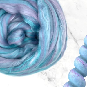 K&ouml;nnte beinhalten: Nahaufnahme eines Kn&auml;uels bunter Wolle in Blau-, T&uuml;rkis- und Lavendelt&ouml;nen. Die Wolle ist weich und flauschig, ideal f&uuml;r Strick- oder H&auml;kelprojekte. Die Farben verschmelzen zu einem sch&ouml;nen, strukturierten Effekt.