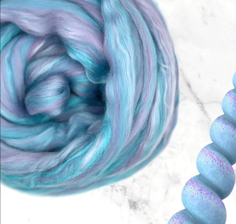 K&ouml;nnte beinhalten: Nahaufnahme eines Kn&auml;uels bunter Wolle in Blau-, T&uuml;rkis- und Lavendelt&ouml;nen. Die Wolle ist weich und flauschig, ideal f&uuml;r Strick- oder H&auml;kelprojekte. Die Farben verschmelzen zu einem sch&ouml;nen, strukturierten Effekt.