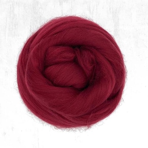 Puede incluir: Primer plano de una bola de vellón de lana rojo oscuro. La lana es suave y esponjosa, perfecta para el fieltro o el hilado.