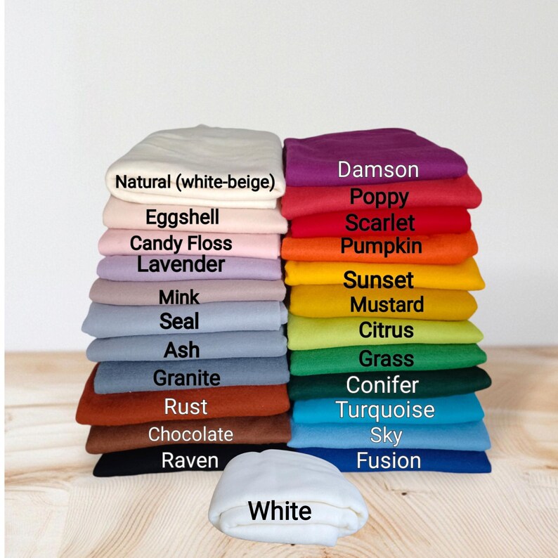 Op de afbeelding: Een stapel gevouwen stoffen in diverse kleuren, gelabeld met tekst waaronder Natural, Eggshell, Candy Floss, Lavender, Mink, Seal, Ash, Granite, Rust, Chocolate, Raven, Damson, Poppy, Scarlet, Pumpkin, Sunset, Mustard, Citrus, Grass, Conifer, Turquoise, Sky, Fusion en White.