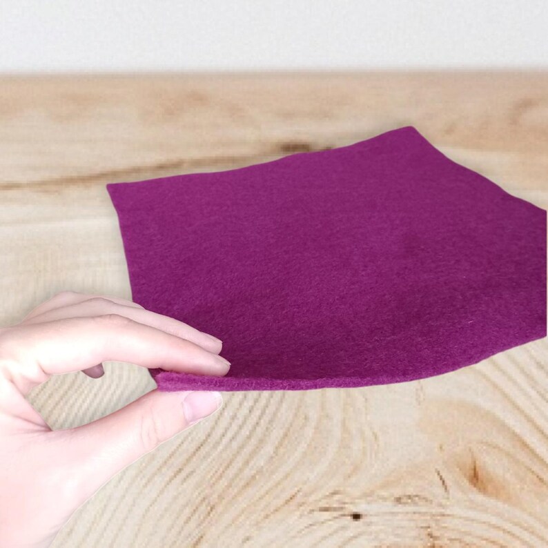 Op de afbeelding: Een vierkant stuk diep magenta vilt met een zachte, matte textuur. Het materiaal is flexibel en heeft een consistente, effen kleur over het gehele oppervlak, met een strakke rand en een gelijkmatige, niet-geweven vezelige uitstraling.