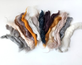 May include: A collection of different colored wool fibers, including white, gray, brown, orange, and dark blue. The fibers are arranged in a fan shape, with the white fibers at the top and the dark blue fibers at the bottom.
