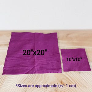 Op de afbeelding: Twee vierkante paarse stoffen naast elkaar. Het grotere stuk is gelabeld 20"x20" en het kleinere stuk 10"x10". De tekst onderaan luidt: *Sizes are approximate (+/- 1 cm). De stof heeft een matte afwerking.