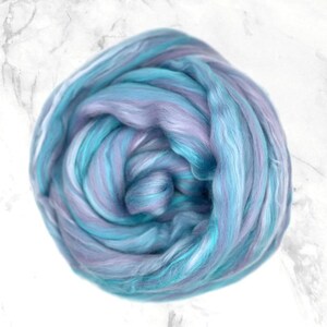 K&ouml;nnte beinhalten: Ein Kn&auml;uel aus Fasern in Blau-, T&uuml;rkis- und Lavendelt&ouml;nen. Die Faser ist eng gewickelt und erzeugt ein wirbelndes Muster. Die Textur wirkt weich und flauschig, geeignet f&uuml;r verschiedene Bastelprojekte.