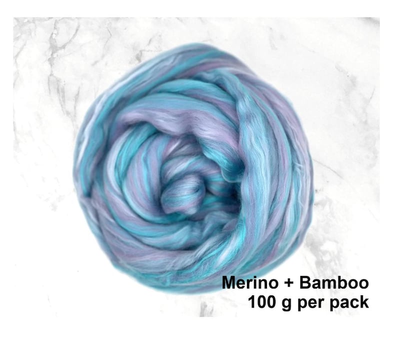 K&ouml;nnte beinhalten: Ein Kn&auml;uel aus Merino- und Bambusfasern in Blau- und Lavendelt&ouml;nen. Die Faser ist eng gewickelt und zeigt eine Mischung aus hellen und dunklen Farbt&ouml;nen. Der Text "Merino + Bamboo 100 g pro Packung" ist sichtbar.