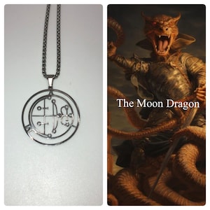 May include: A silver necklace with a circular pendant featuring a detailed, intricate design. The pendant is a sigil, a symbol used in magic and ritual. The necklace is on a white background. The image also shows a fantasy illustration of a dragon with the text "The Moon Dragon".