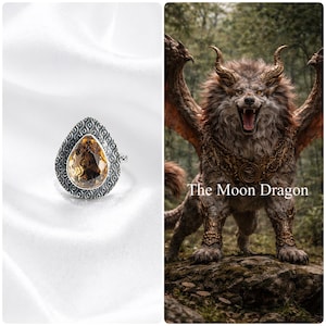 May include: A silver ring with a pear-shaped, amber-colored gemstone. The ring has a detailed, patterned border. The image also features a fantasy illustration of a dragon-like creature with the text "The Moon Dragon".