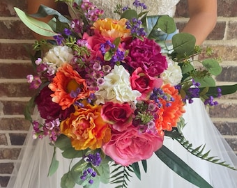 May include: A bridal bouquet with a variety of flowers in shades of pink, orange, and white. The bouquet includes roses, carnations, and other small flowers. The bouquet is held by a person wearing a white wedding dress.