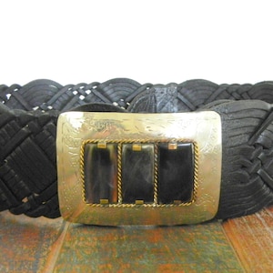 May include: A black leather belt with a woven design and a silver buckle with three black rectangular stones.