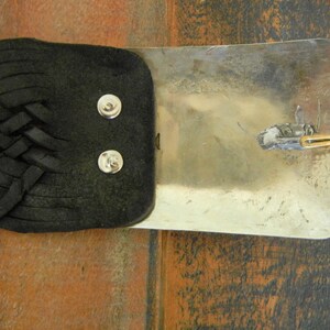 May include: A black leather belt with a silver buckle. The buckle has a braided design and a small metal loop.