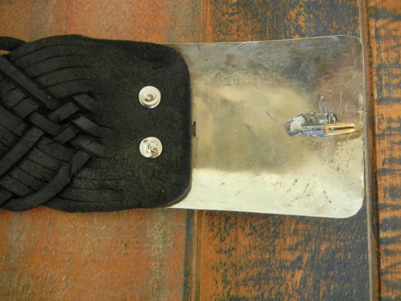 May include: A black leather belt with a silver buckle. The buckle has a braided design and a small metal loop.