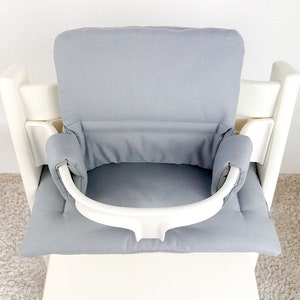 May include: A gray high chair cushion with a white safety strap. The cushion has a padded back and a padded seat.