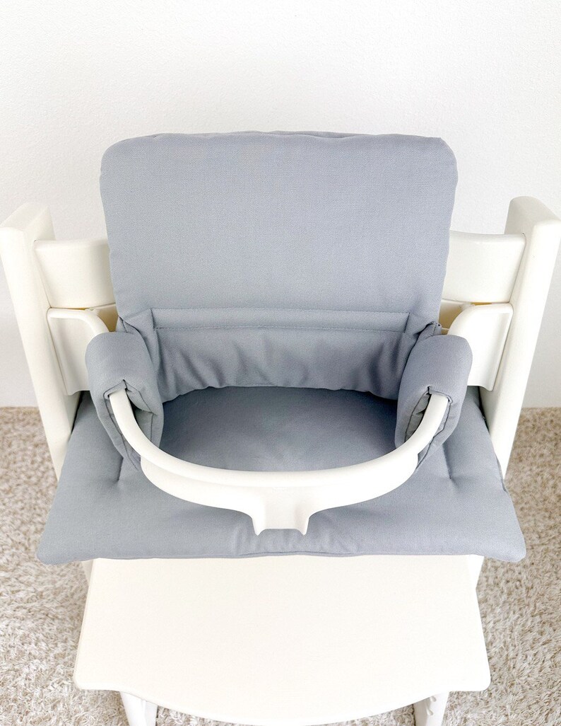 May include: A gray high chair cushion with a white safety strap. The cushion has a padded back and a padded seat.
