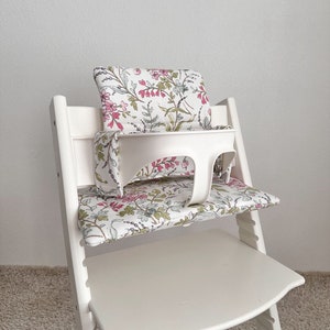 Puede incluir: Silla alta blanca con un coj&iacute;n de estampado floral y una bandeja blanca. El coj&iacute;n tiene un estampado floral rosa, verde y blanco.