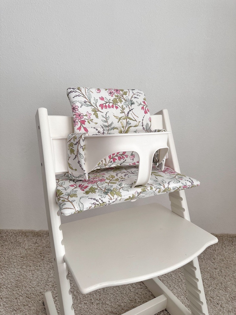 Puede incluir: Silla alta blanca con un coj&iacute;n de estampado floral y una bandeja blanca. El coj&iacute;n tiene un estampado floral rosa, verde y blanco.