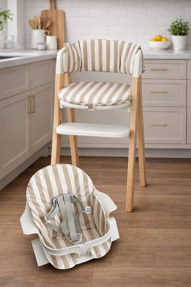 May include: A modern high chair with a wooden frame and white accents. The seat and backrest feature a beige and white striped pattern. An additional seat with the same pattern is placed on the floor. The high chair is designed for infants and toddlers.