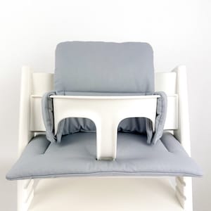 May include: A white high chair with a gray padded seat and back. The chair has a white tray with a gray padded insert.