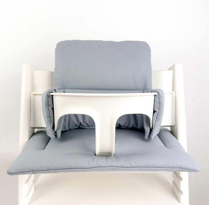 May include: A white high chair with a gray padded seat and back. The chair has a white tray with a gray padded insert.