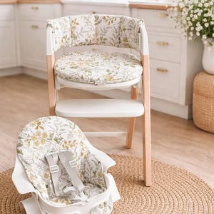 May include: A white high chair with a wooden frame and a floral patterned seat and backrest. A matching infant seat with safety straps sits on a woven mat. The floral pattern includes yellow and green leaves on a white background.