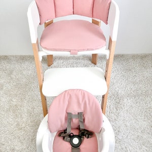 May include: A pink padded high chair with a white frame and a tray. The chair has a five-point harness and a removable tray.