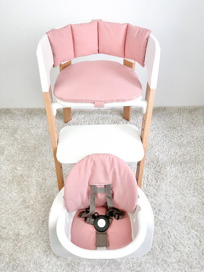 May include: A pink padded high chair with a white frame and a tray. The chair has a five-point harness and a removable tray.