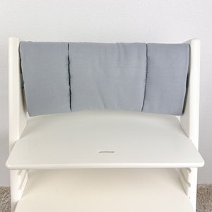 May include: White wooden high chair with a gray padded backrest and a white tray. The chair has a step stool and is designed for children.