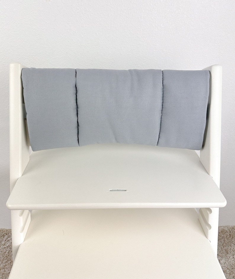 May include: White wooden high chair with a gray padded backrest and a white tray. The chair has a step stool and is designed for children.