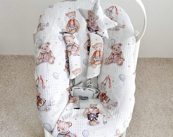 May include: White high chair cushion with a teddy bear pattern. The cushion has a waffle texture and features illustrations of teddy bears in various outfits, along with balloons. A star-shaped toy hangs from the top.
