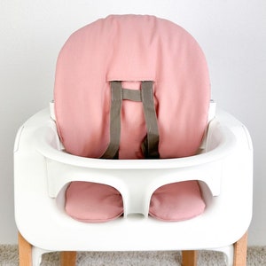 May include: A white high chair with a pink padded seat and back. The chair has a removable tray and a five-point harness.
