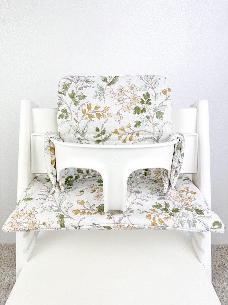 Puede incluir: Una silla alta blanca con un coj&iacute;n estampado floral. El coj&iacute;n tiene un fondo blanco con flores verdes, amarillas y moradas.