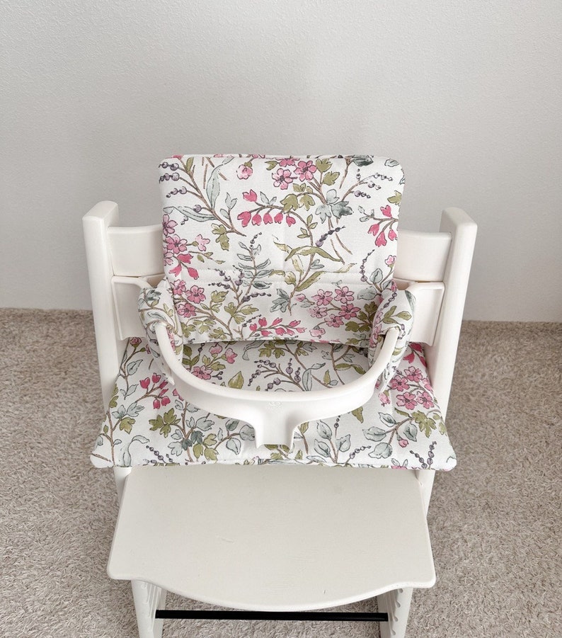 Puede incluir: Silla alta blanca con un coj&iacute;n estampado floral y una bandeja blanca. El coj&iacute;n tiene un estampado floral rosa y verde.