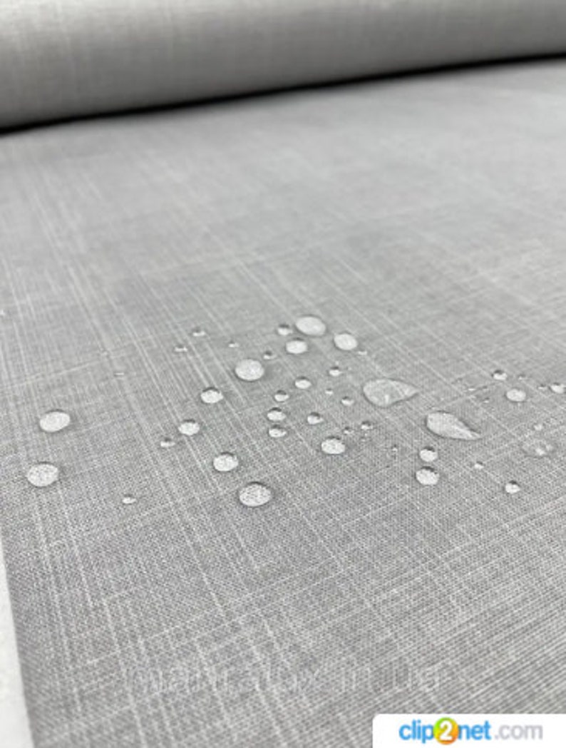 May include: Close-up of a roll of gray fabric with a textured surface. Water droplets are scattered across the fabric, indicating a waterproof or water-resistant quality. The fabric has a subtle, woven pattern.