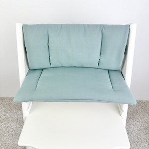 K&ouml;nnte beinhalten: Ein wei&szlig;er Hochstuhl mit einem hellblauen gepolsterten Sitz und R&uuml;ckenlehne. Der Stuhl hat ein wei&szlig;es Tablett.