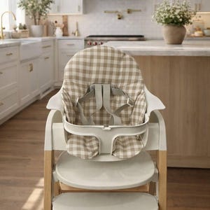 May include: A modern high chair with a beige and white checkered seat and safety straps. The chair has a white frame with wooden legs and two footrests. The high chair is designed for infants and toddlers.