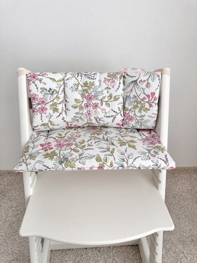 Puede incluir: Silla alta blanca con un coj&iacute;n de estampado floral. El coj&iacute;n est&aacute; hecho de tela con flores rosas y verdes sobre un fondo blanco.