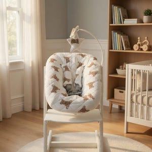 May include: A white high chair with a padded seat featuring a teddy bear pattern. The chair has a safety harness and a mobile with a star and teddy bear. The chair is on a white rug in a room with a bookshelf and crib.